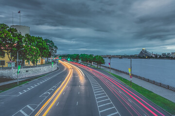 Long exposure photo of car light trails in windy and cloudy weather next to river 