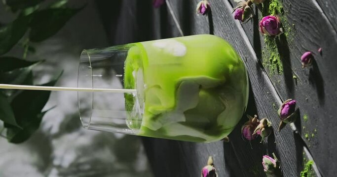 Preparing matcha latte, pouring milk in a glass with green tea and ice cubes, preparing a cool refreshing drink with powdered green tea, slow motion close-up video, high quality 4k footage