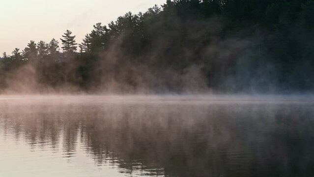 Morning fog moving across a reflective lake at sunrise with an forested island in the background