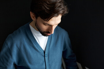 Obraz premium Sad upset bearded handsome young man having troubles at work, failed in business project or lost big sum of money investing at stock trading market, looking down against black background