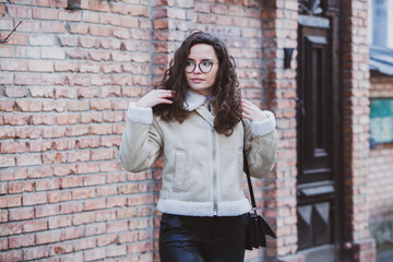 Beautiful young woman with brunette curly hair, portrait in eye glasses enjoying the sun in the city.
