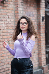 Beautiful young woman with brunette curly hair, portrait in eye glasses enjoying the sun in the city.