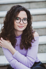 Beautiful young woman with brunette curly hair, portrait in eye glasses enjoying the sun in the city.