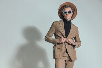 cool blonde hair man with hat and sunglasses buttoning beige suit