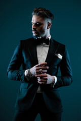 attractive bearded man in elegant tuxedo looking to side and touching fingers