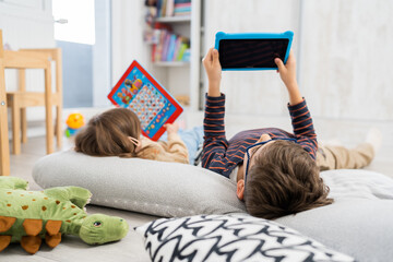 Two children brother and sister playing at home with tablet and laying on the floor