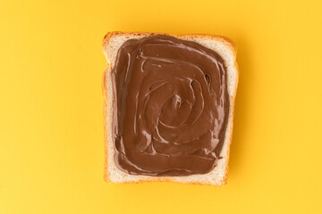 Top view of white toast bread with chocolate hazelnut spread on the yellow background. Morning breakfast concept. Food mockup with copy space for a free text. Flat lay.