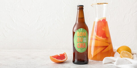 Bottle and jug of tasty citrus kombucha on light background with space for text