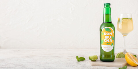 Bottle and glass of tasty kombucha on light background with space for text