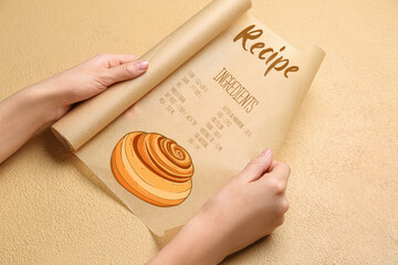 Female hands holding baking paper with written recipe on beige background