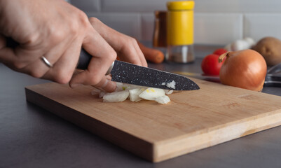 Hands with knife cutting an onion on a cutting board. Kitchen background, cooking concept, cutting vegetables. 