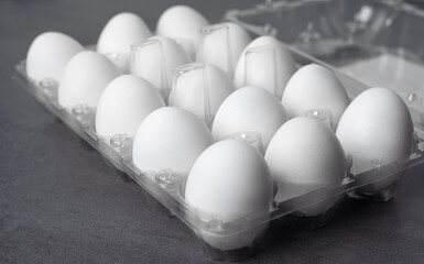 Plastic egg tray with fifteen white eggs close up on a grey textured background