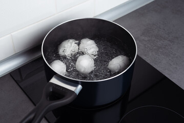 A pan with some boiling eggs on a stove. White eggs in boiling water. Cooking process.