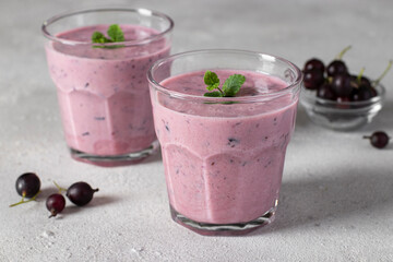 Smoothie from natural yogurt and black currant in two glass on light gray background