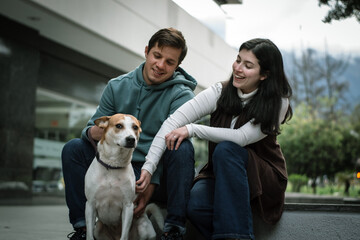 Happy couple with their dog sitting in front of a building in the city. Happy dog with his family in the city. The dog receives love from his family