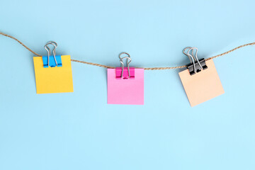 Sticky notes with binder clips hanging on rope against color background
