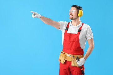 Male carpenter in hearing protectors pointing at something on blue background