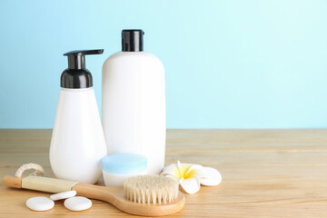 Cosmetic products, massage brush and spa stones on wooden table against color background