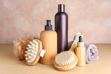 Bottles of cosmetic products, massage brushes, sponge and towel on color background