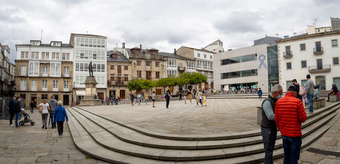 Plaza Mayor de Viveiro en Lugo, con gente paseando, dia nublado y edificios con árboles verdes y...