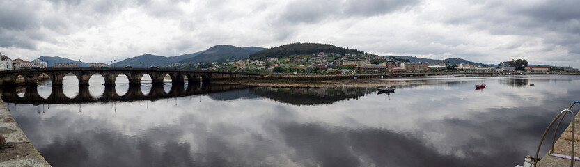 Obraz premium Vista panorámica de la ria de Vicedo en Lugo con vistas del viejo puente y nubes reflejadas en el agua del río, en Galicia, verano de 2021