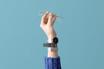 Woman with stylish wristwatch and eyeglasses on blue background