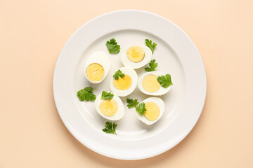 Plate with halves of delicious boiled eggs and parsley on beige background