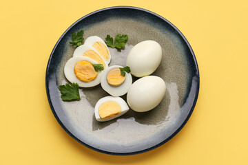 Plate with delicious boiled eggs and parsley on yellow background