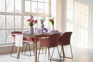 Beautiful table setting for International Women's Day celebration with different flowers and burning candles in light room near window