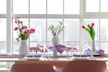 Beautiful table setting for International Women's Day celebration with different flowers and burning candles in light room near window