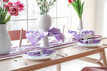 Beautiful table setting for International Women's Day celebration with different flowers and burning candles in light room near window