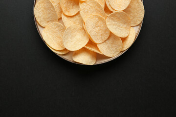 Plate with delicious potato chips on black background