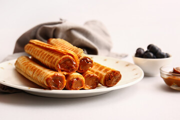 Plate of delicious wafer rolls with boiled condensed milk on white background