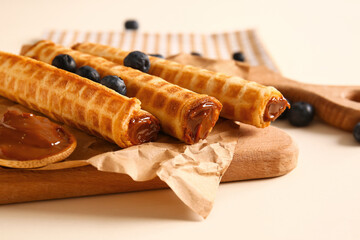 Delicious wafer rolls with boiled condensed milk and blueberries on beige background, closeup