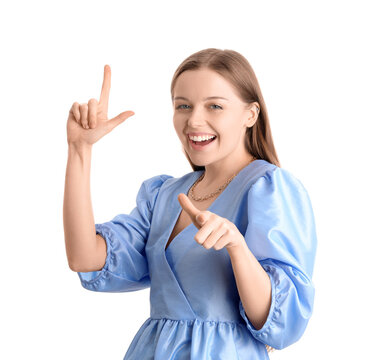 Young woman in dress showing loser gesture and pointing at viewer on white background