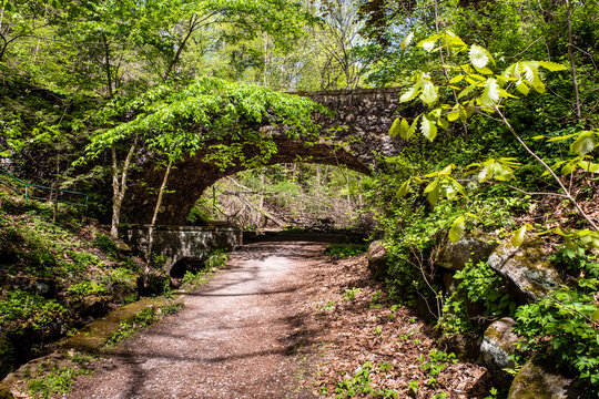 Stone bridge embedded in the green vegetation with a gravel path underneath in Shenley Park, Pittsburgh, Pennsylvania.