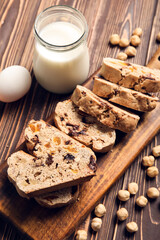 Board with delicious biscotti cookies, milk and hazelnuts on brown wooden background