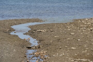 Tributary stream of a lake on the dried up bottom of soil. A sign of water scarcity that diminishes the body of water. Suitable as background with ecology themes with copy space. 