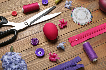 Fototapeta na wymiar Sewing supplies with Easter eggs and flowers on wooden background, closeup