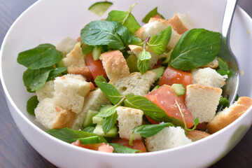 Bread salad with cucumber, tomatoes, and mint in a white bowl. 