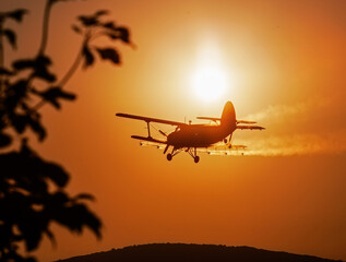 Silhouette of classic agricultural biplane fly at sunset and spraying chemicals