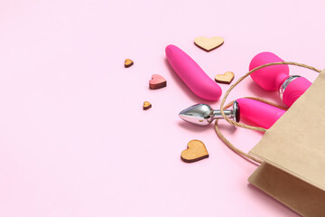 Shopping bag with sex toys and wooden hearts on pink background