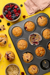 Whole grain fruity muffins with blueberries and strawberries in a metal mold on a yellow background. Healthy berry dessert. Top view