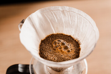 Pour over filter with ground coffee in the funnel in focus. Drip filter coffee brewing. Pour over alternative method of pouring water over roasted and ground coffee beans contained in filter.