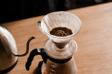 Pour over filter with ground coffee in the funnel in focus. Drip filter coffee brewing. Pour over alternative method of pouring water over roasted and ground coffee beans contained in filter.