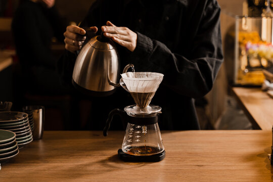 Pour over filter coffee alternative brewing method. Pouring hot water over roasted and ground coffee beans contained in paper filter.
