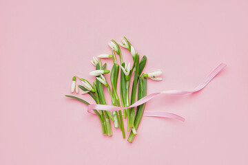 Bouquet of beautiful snowdrops with ribbon on pink background