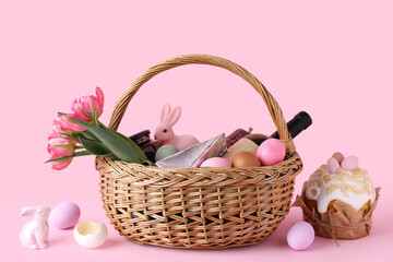 Basket with Easter eggs, tulip flowers and bottle of wine on pink background