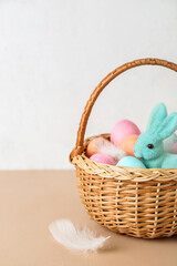 Basket with Easter eggs and bunny on beige table against white background