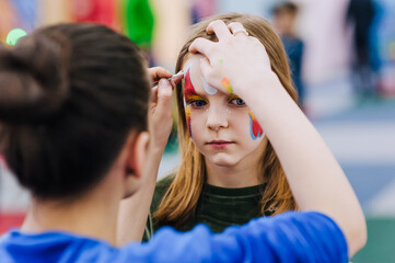 A professional make-up artist, woman artist paints face painting on her face with paints, children's makeup for a little girl, child. Photography, art, creativity concept, lifestyle.